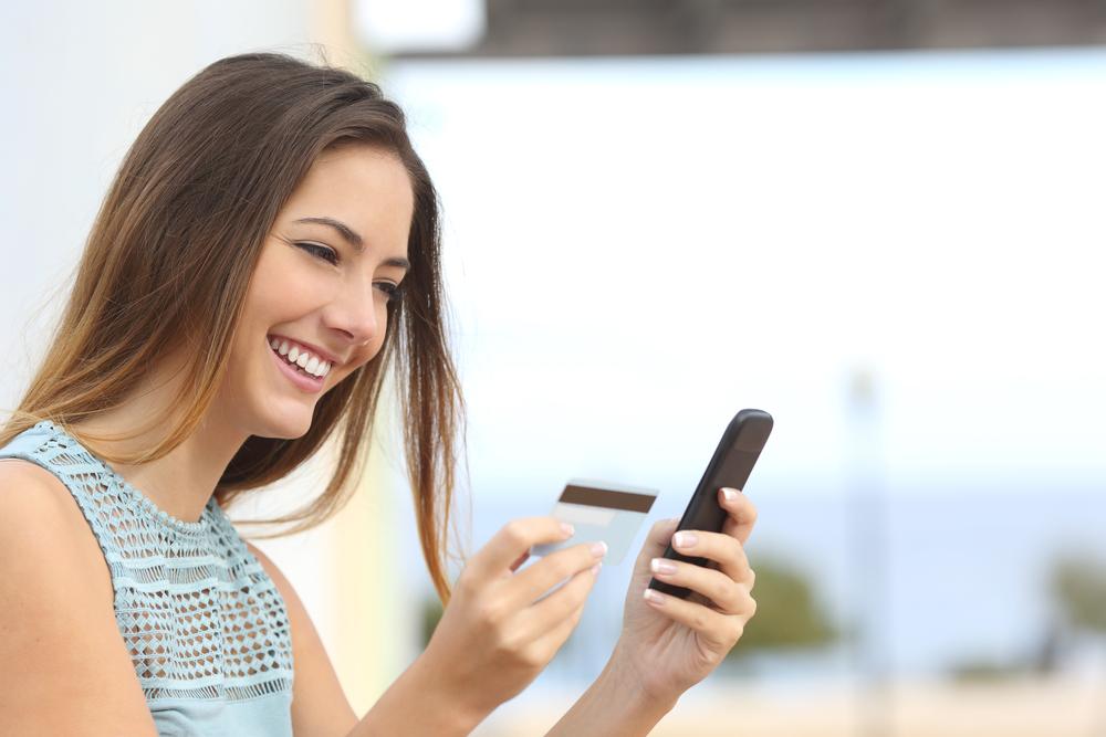Frau hlt Smartphone in der einen und Kreditkarte in der anderen Hand